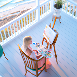  Create a light and airy portrait of a blonde woman sitting in a big chair, painting on a large canvas. She is surrounded by paintbrushes and paints. In the top floor of a house with big french double doors opening to a deck overlooking the ocean. The mood is light and airy, with pastel colors.